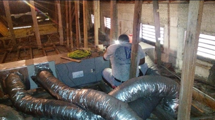 Worker in an attic installing flexible silver ductwork around a central air handler