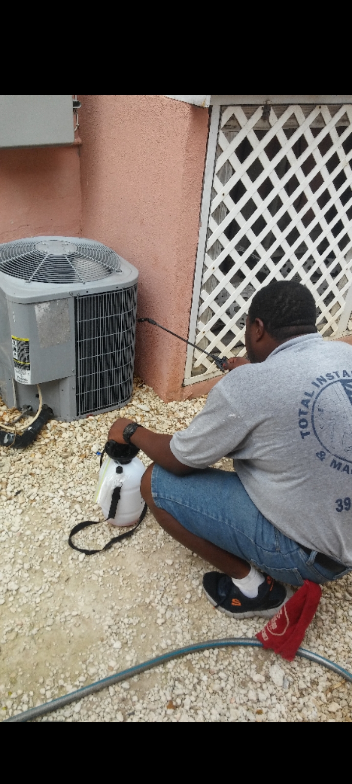Technician in a Total Installation crew shirt servicing an outdoor AC condenser