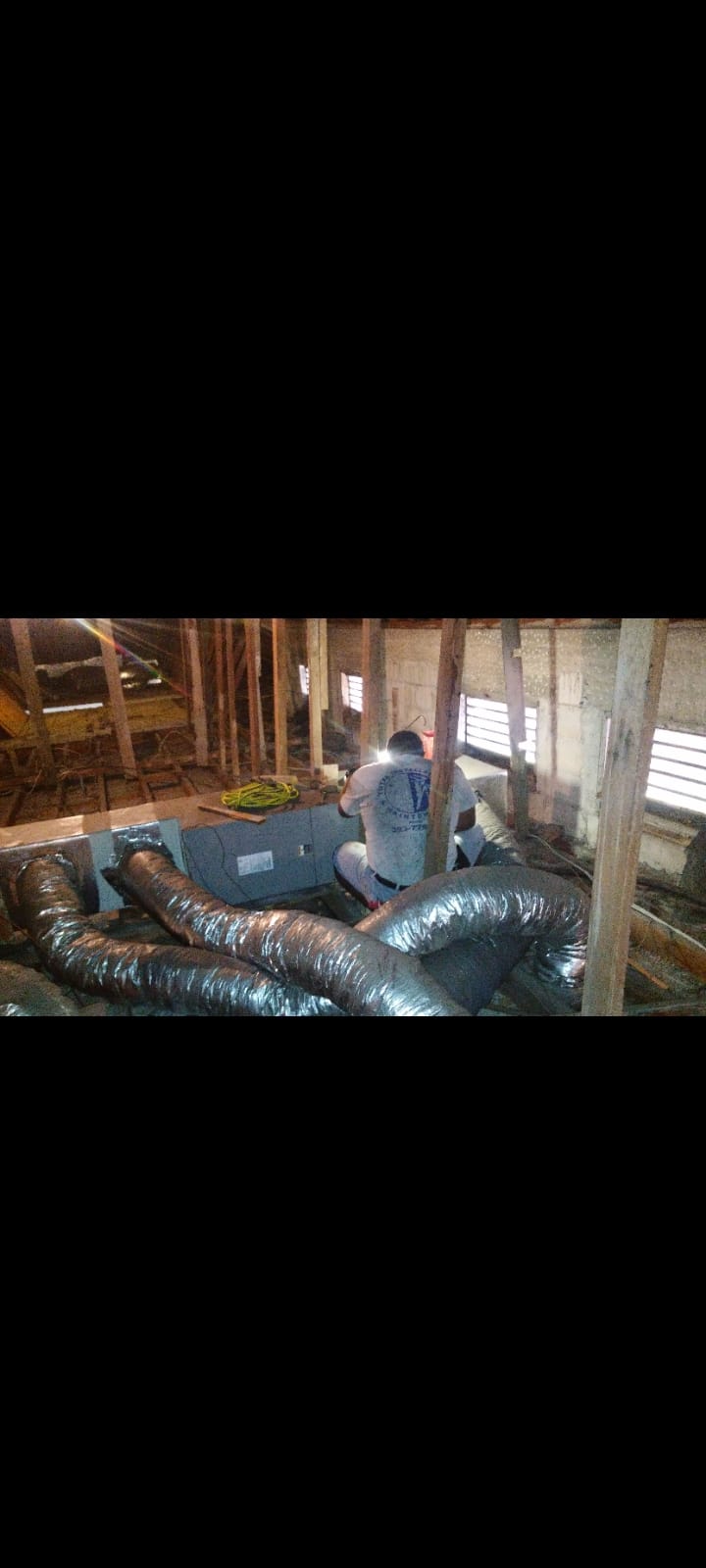 Worker in an attic running flexible silver duct around a central air handler