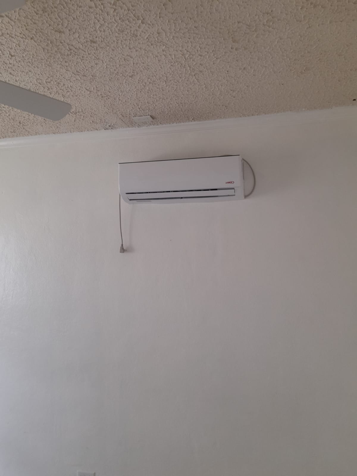 Outdoor Lennox AC condenser installed and running on a wall-mounted bracket
