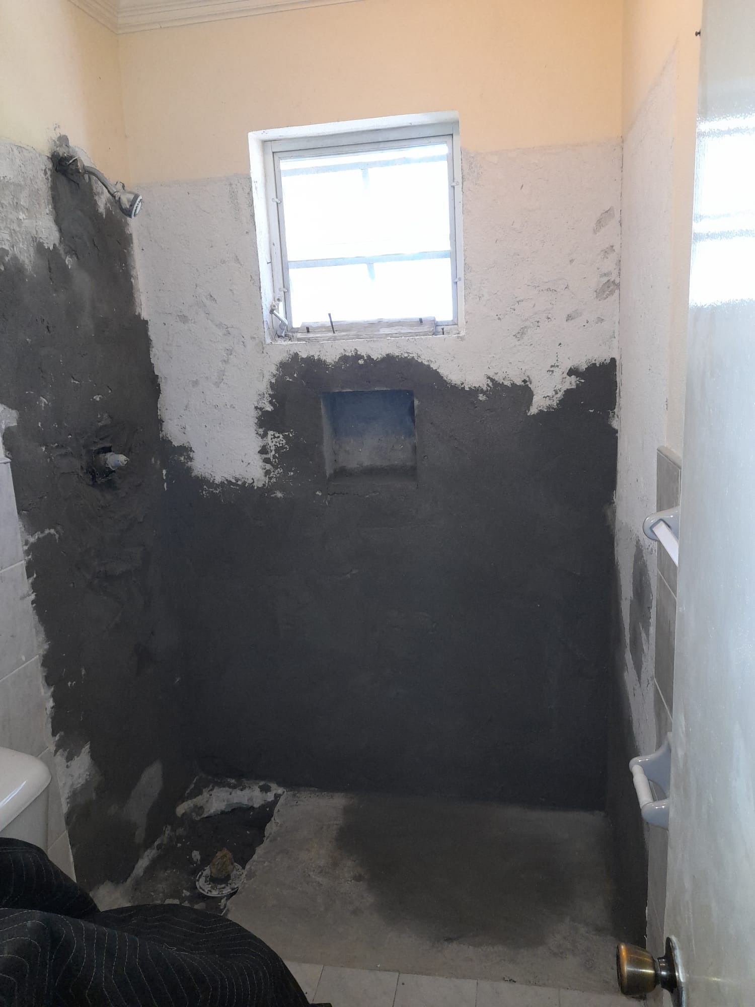 Bathroom shower stall stripped down with dark waterproof base coat applied, recessed niche cut into the back wall