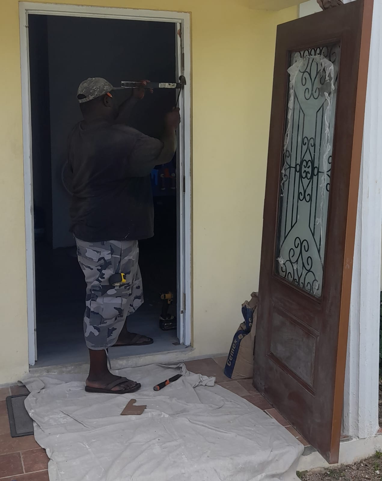 Worker chiseling a hinge mortise in a door frame, the new wood door with iron grill leaning beside him
