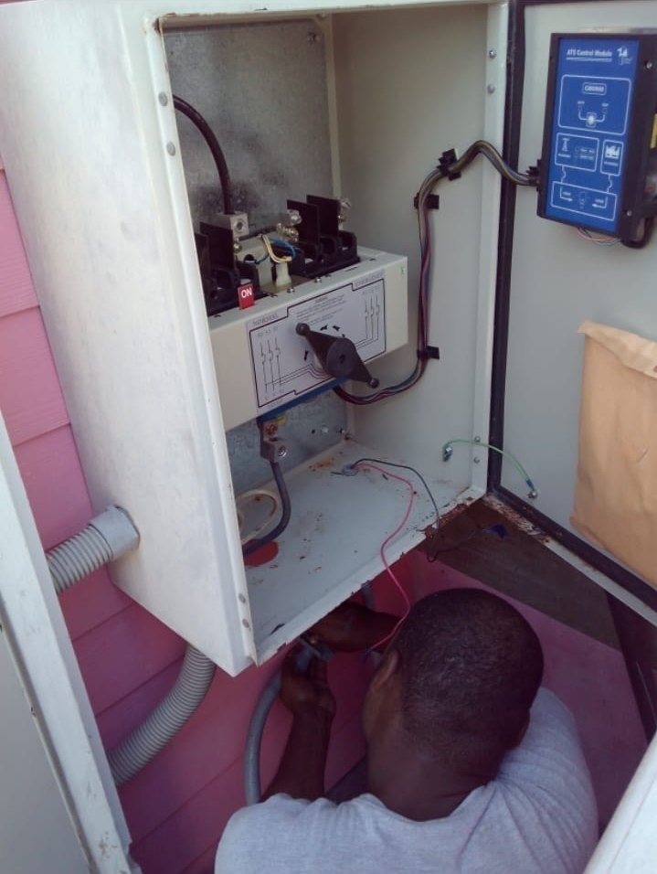 Crew member wiring an automatic transfer switch panel with a control module on the side