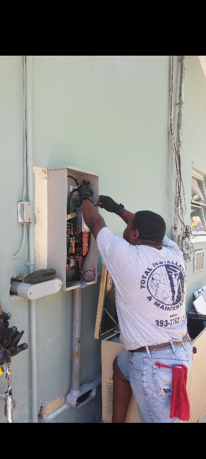 Crew member in a Total Installation shirt wiring an outdoor main service panel