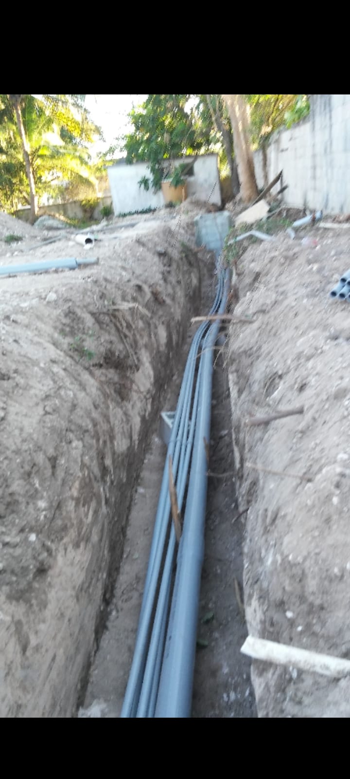 Long deep trench with multiple gray PVC conduits running underground for an electrical service
