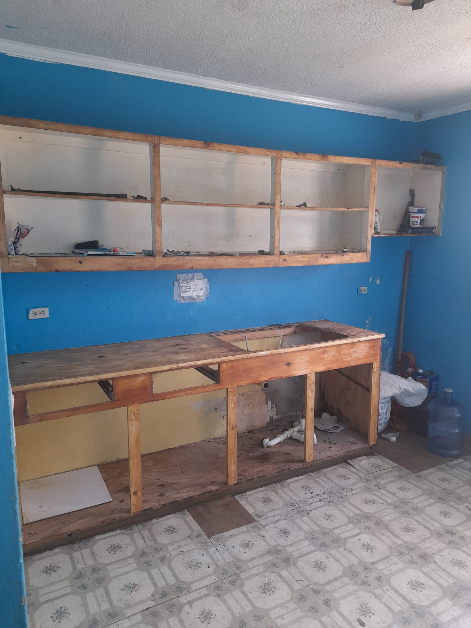 Gutted kitchen with blue painted walls, stripped open cabinets, and old patterned tile floor