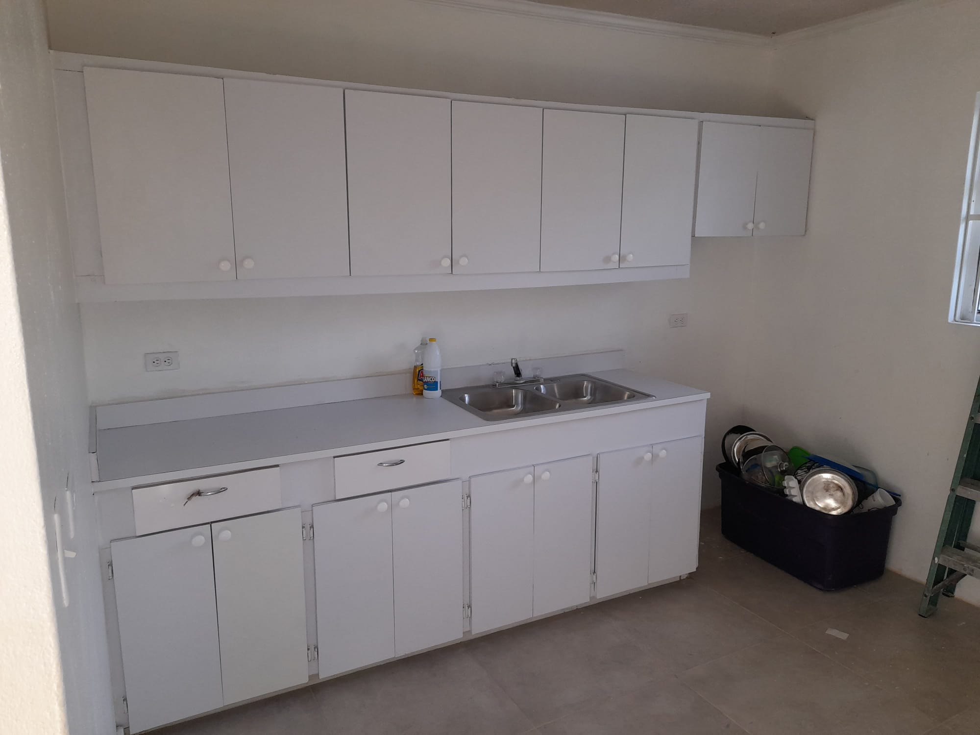 Kitchen cabinets primed white with stainless double sink installed and counter set, no doors yet