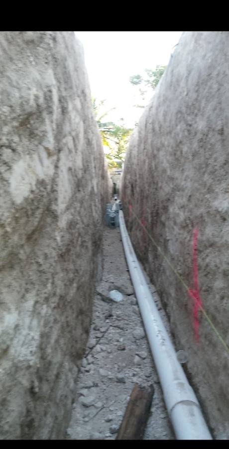 Deep narrow trench cut between rock walls with a white PVC drain line laid along the bottom