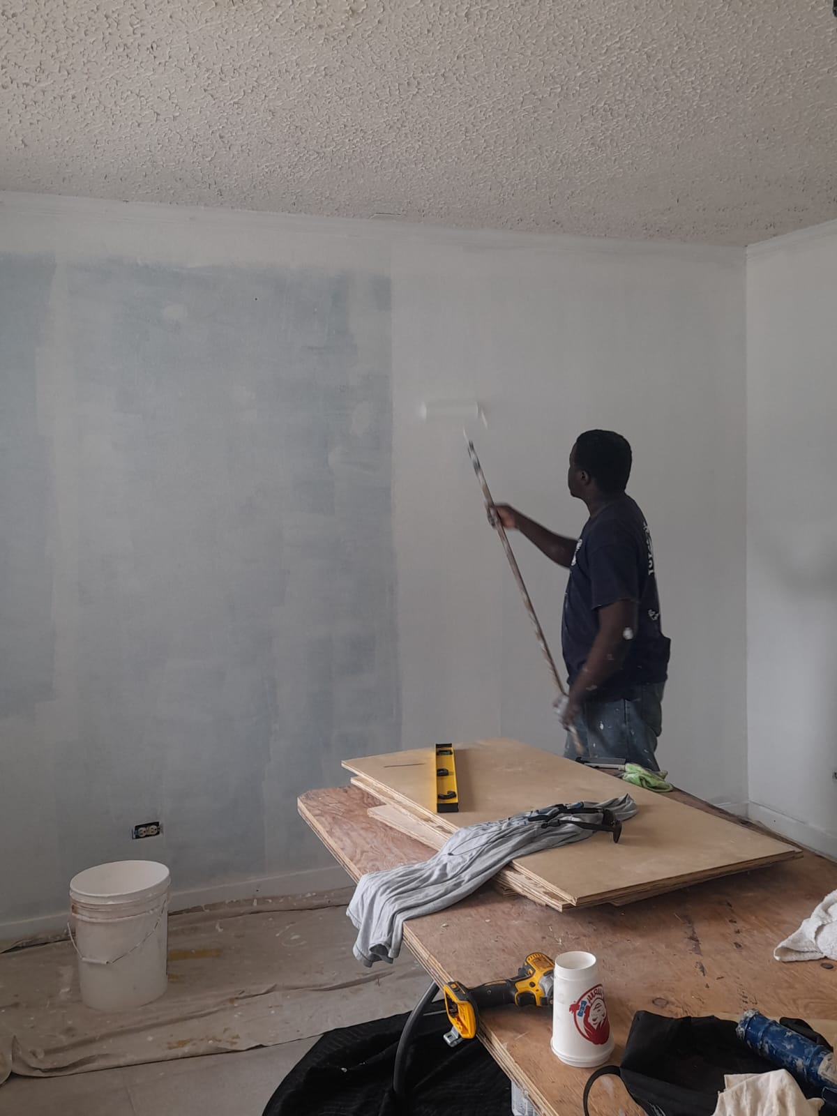 Worker rolling primer on a patched interior wall using an extension pole