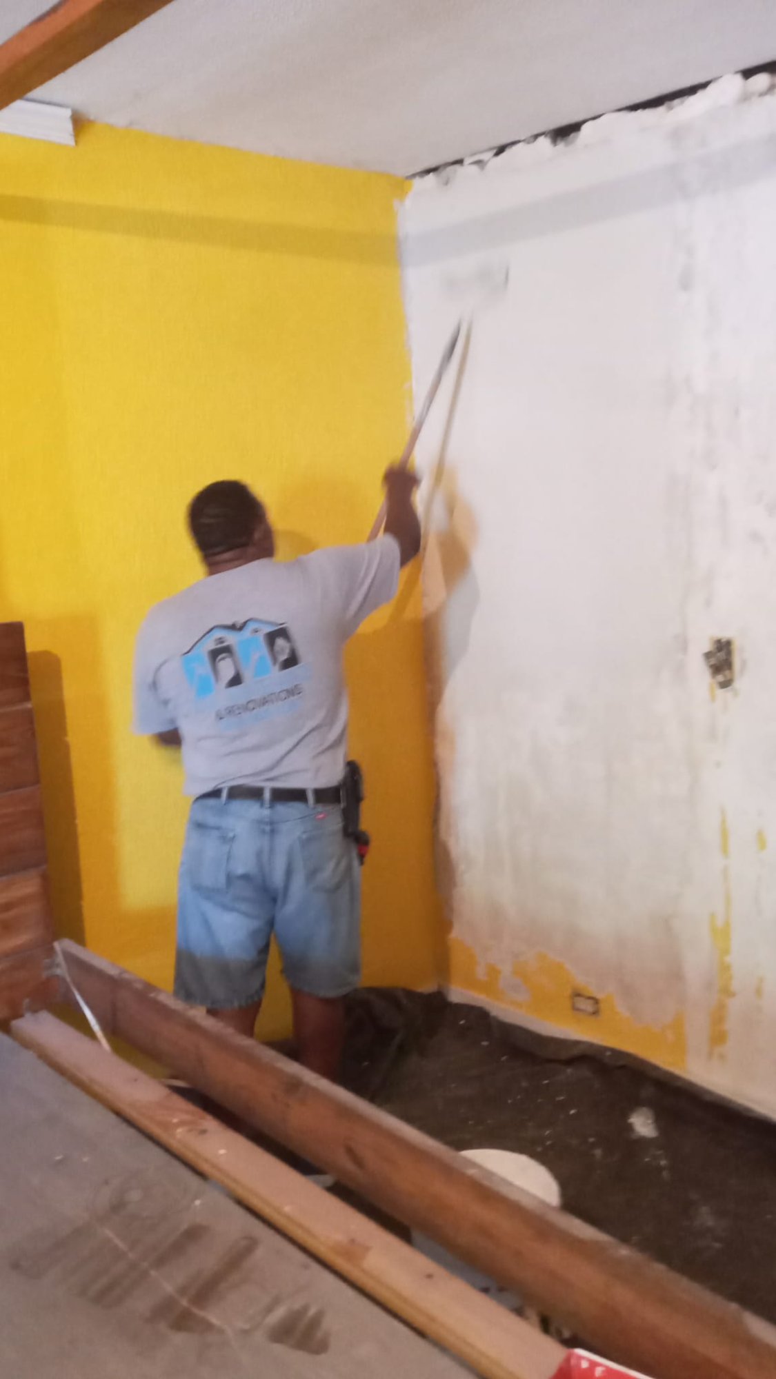 Crew member rolling primer on a wall next to a finished, warm-yellow painted wall