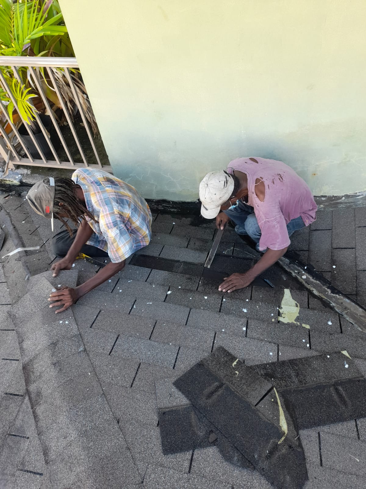 Two roofers laying shingles tight to a stucco wall during a flashing replacement