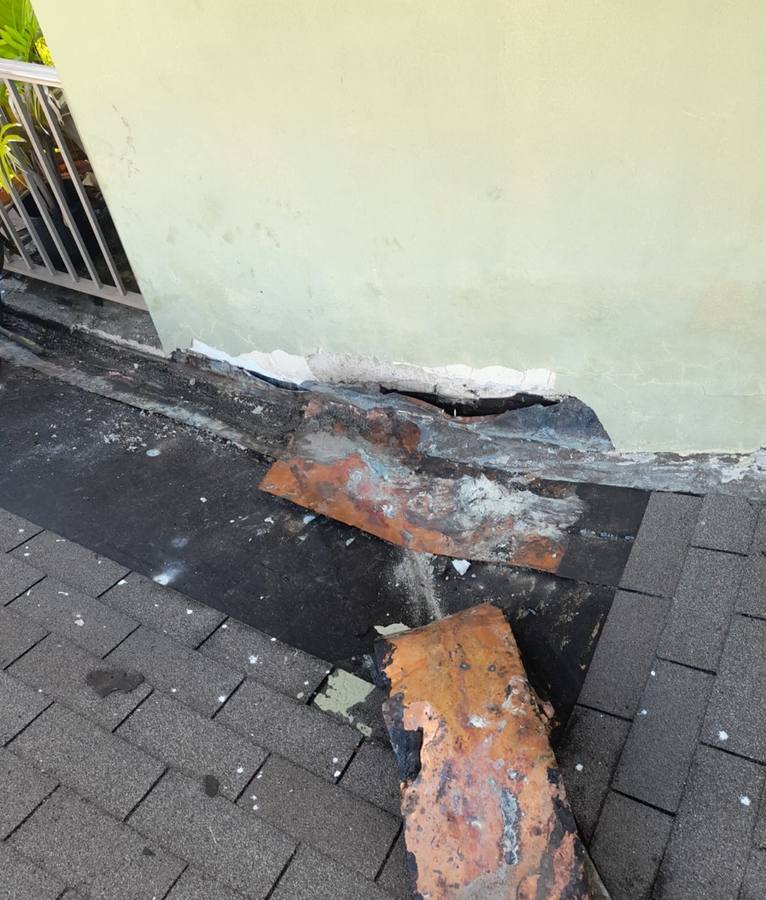 Roof before repair, heavily rusted metal flashing peeling at the wall edge