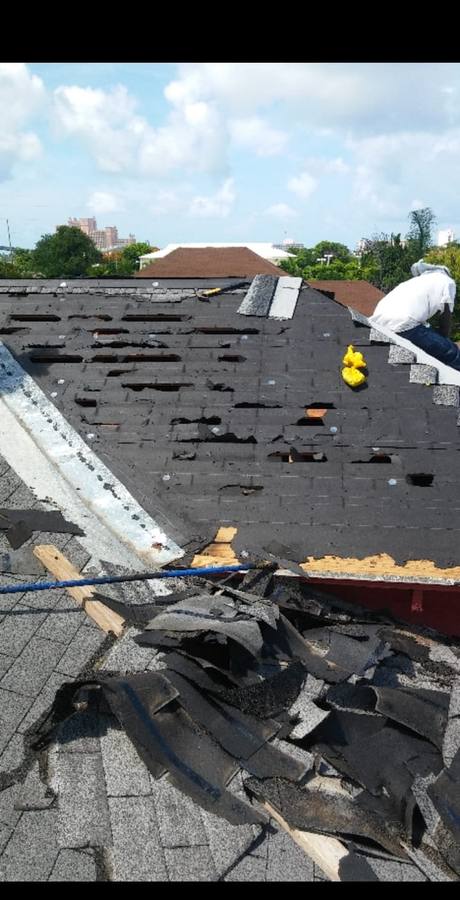 Storm-damaged roof torn open with multiple holes through old shingles, debris piled below