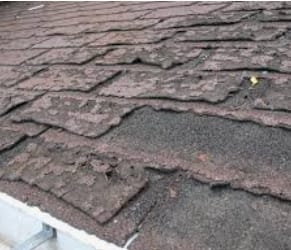 Close-up of badly worn, curling shingles at a roof edge
