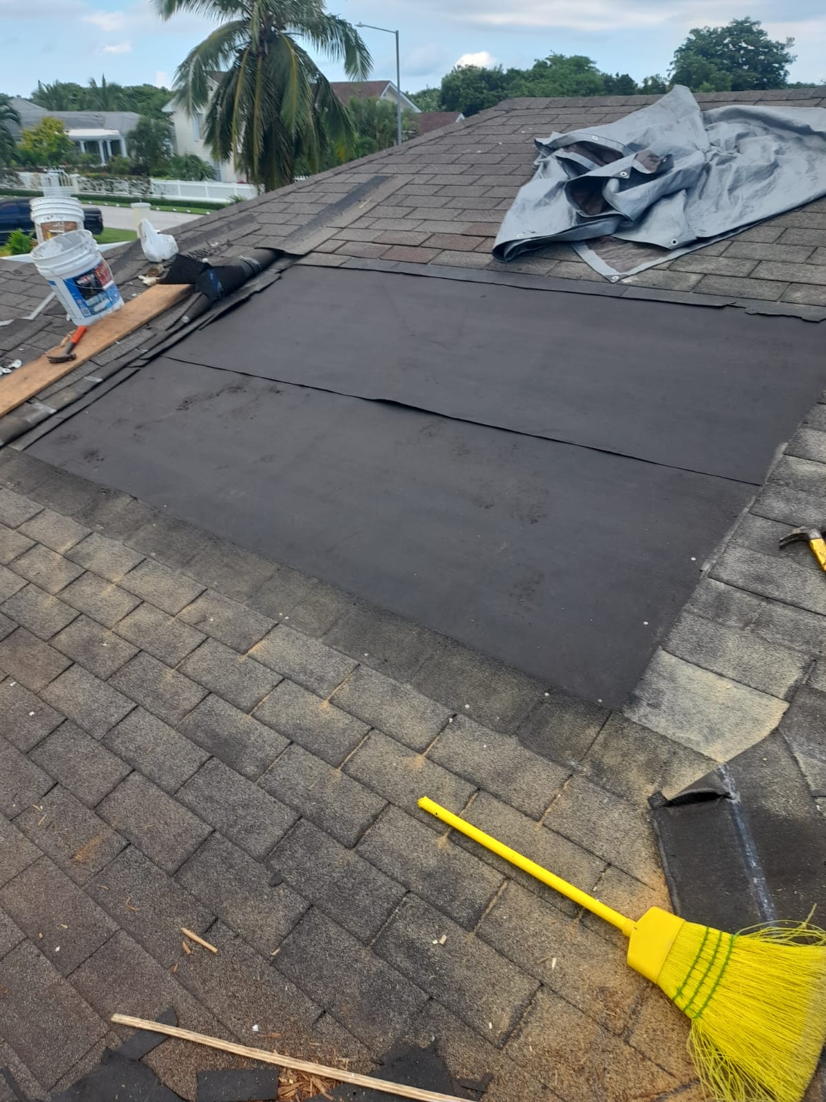 Fresh black underlayment laid over a new plywood patch, surrounded by existing shingles